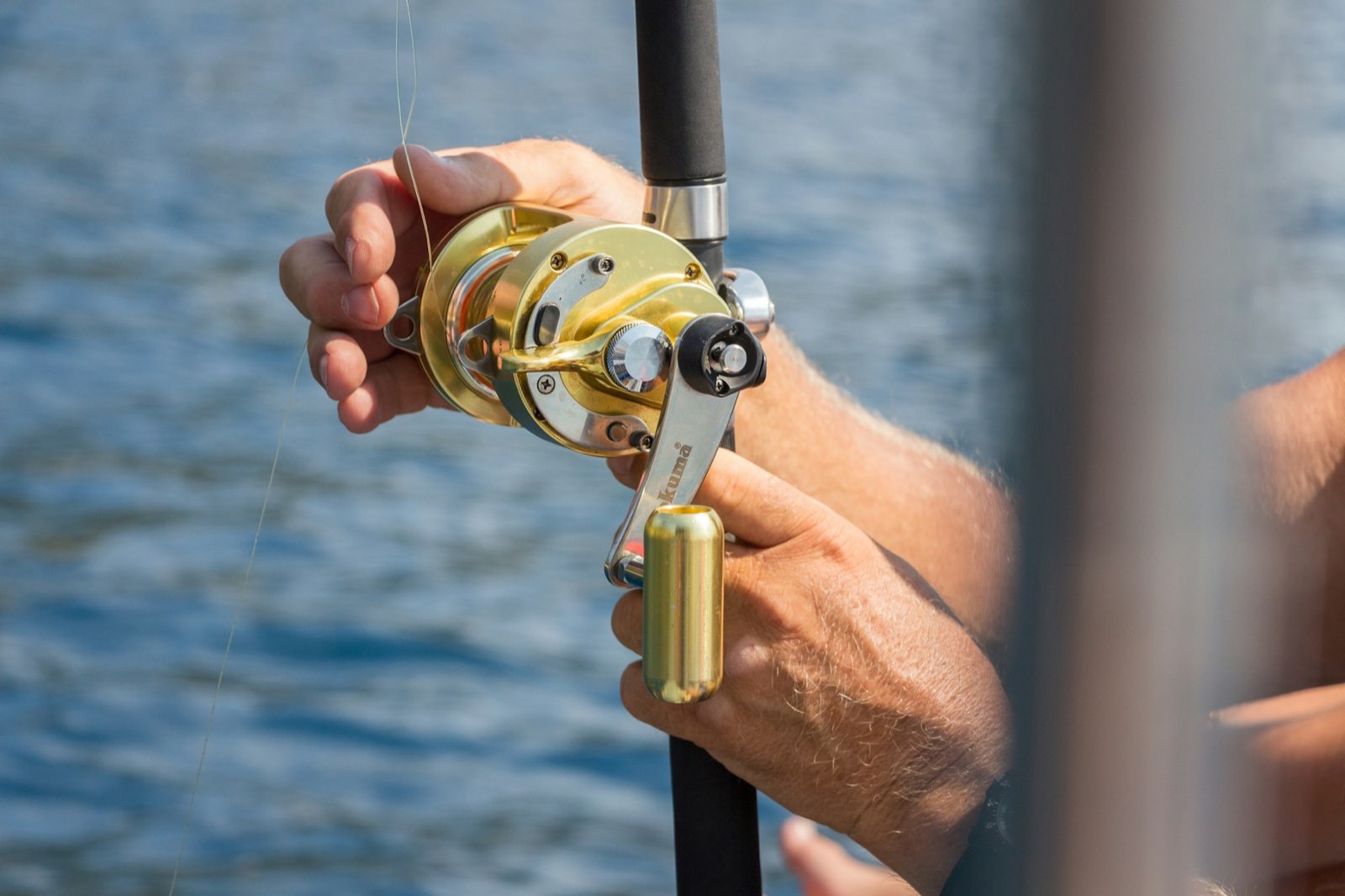A trolling reel in an angler’s hands over blue water (stock photo)